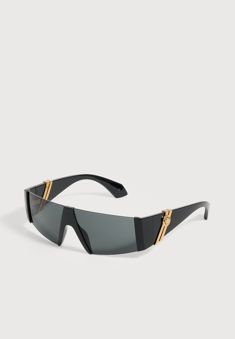 Lunettes de soleil enveloppantes noires avec verres teintés foncés et accents décoratifs dorés sur les branches.