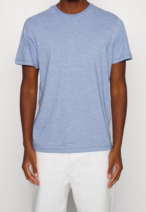 Light blue cotton T-shirt with short sleeves, round neckline, and a textured finish. Worn with white pants, displaying a casual fit.
