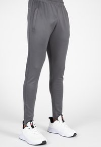 Grijze sportbroek van glad, lichtgewicht stof. Voorzien van zijzakken, een taps toelopende pasvorm en een elastische tailleband. Gepaard met witte sneakers.