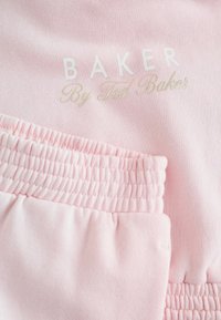 Tela de algodón de color rosa claro con el texto "BAKER By Ted Baker" en blanco y dorado, con detalles elásticos fruncidos en la cintura.