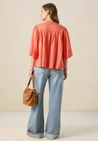 Blouse corail à manches bouffantes, coupe ample et design carré, associée à un jean léger bleu clair à jambes larges et un sac à bandoulière en suède beige.