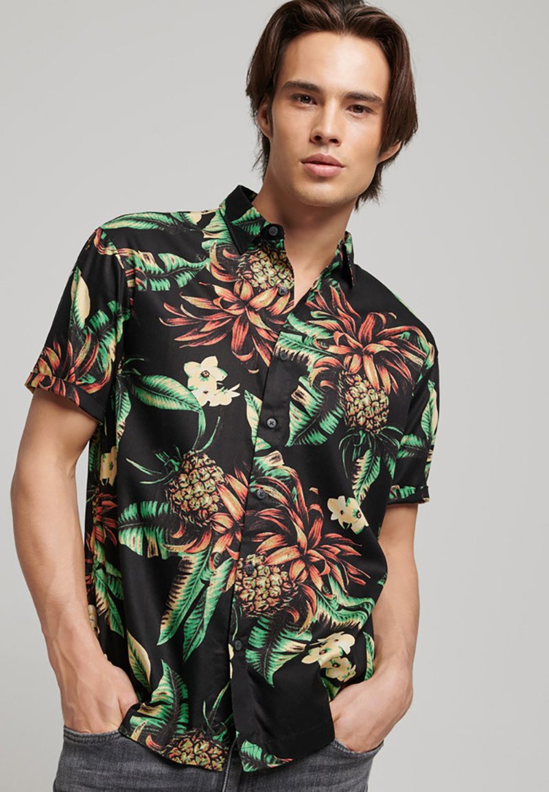 Camicia a maniche corte con bottoni nera caratterizzata da un vivace motivo floreale tropicale e ananas in verde, arancione e giallo su un tessuto liscio.