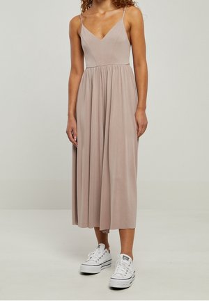 Lichtbeige jurk met een v-hals, spaghetti bandjes en een vloeiende rok, gecombineerd met witte sneakers. Zachte, gladde stoftextuur.