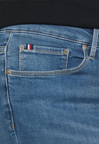 Jasnoniebieskie dżinsy z małą czerwoną, białą i niebieską metką na tylniej kieszeni, widocznymi szwami i gładką teksturą.