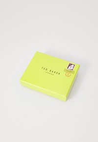 Geel, textuurdoos met een gouden logo "TED BAKER LONDON" op de voorkant, met een postzegelontwerp in de rechterbovenhoek.
