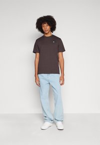 Svart bomull T-skjorte med korte ermer, med en liten blå logo på brystet. Kombinert med lyseblå jeans og hvite sko.