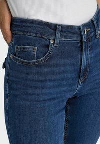 Jeans denim w ciemnoniebieskim kolorze, z klasycznym pięciopocketowym wzorem, zapięcie na guzik i zamek błyskawiczny oraz widocznymi detalami w szyciu.