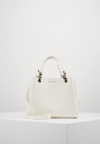Vit läderhandväska med en strukturerad design, topphandtag och en avtagbar axelrem. Märkbara metalldetaljer och varumärkesprägling.