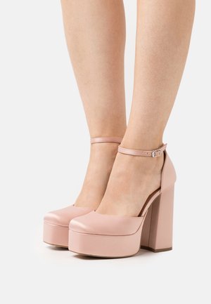 Talons compensés en cuir verni rose avec un bout arrondi, une bride de cheville et un talon épais. Texture lisse avec une finition brillante.