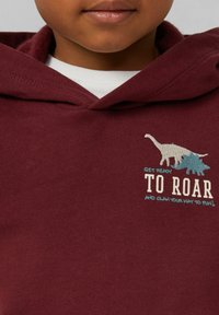 Bordeaux hoodie van zacht materiaal met een kangoeroezak, met een dinosaurustekening en de tekst "BEREID JE VOOR OM TE BRAULLEN," in wit en blauw.