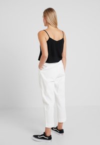 Camisole noire cropped avec des fines bretelles, associée à un pantalon blanc taille haute. Des baskets en toile noires complètent la tenue.