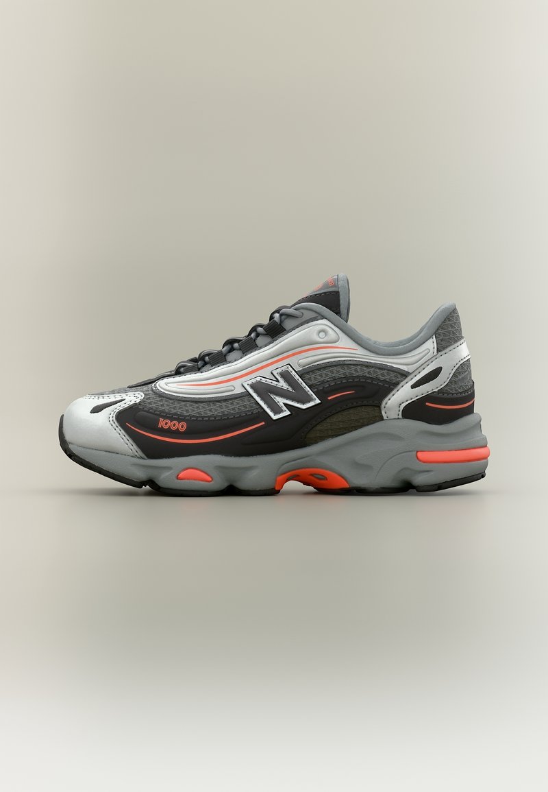 Baskets New Balance grises et noires avec des accents orange et le logo "1000", vues de côté sur un fond uni.