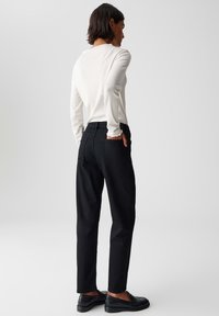 Pantaloni neri con vestibilità a gamba dritta, realizzati in tessuto misto cotone. Abbinati a una maglia leggera a maniche lunghe e mocassini neri.