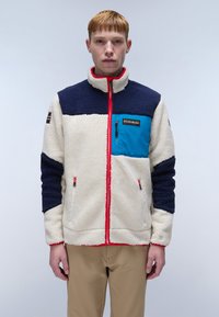 Fleece jacket in cream, navy, and blue with red accents; high collar, zip pockets, textured material, and brand logo on chest.