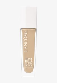 Lancôme foundationflaske med et rektangulært klart glasshus, beige væske indeni og et slankt hvidt låg. Etiketten lyder "Teint Idole Ultra Wear."