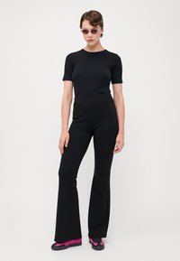 Haut noir ajusté à manches courtes associé à un pantalon noir évasé à taille haute. Les accessoires comprennent des lunettes de soleil roses et des chaussures de sport noires avec des accents roses.