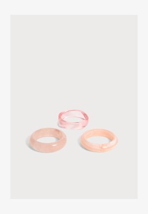 Tre glatte pastelresinringe i rosa og fersken nuancer arrangeret på en ensfarvet lysegrå baggrund.