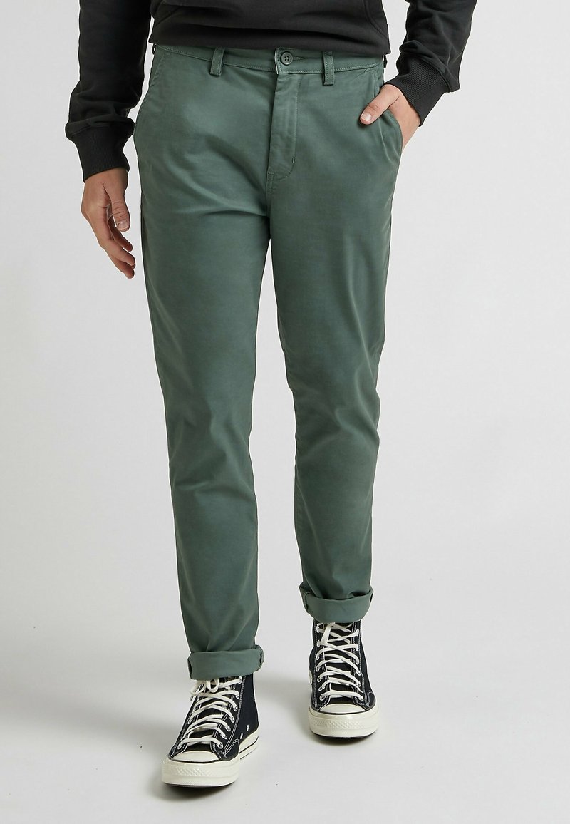 Pantalon en coton vert slim avec ourlets roulés, doté de poches latérales et d'un devant plat, associé à des baskets montantes noires.