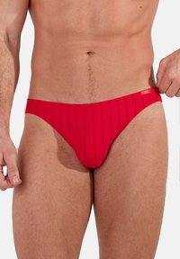 Slip de bain à rayures rouges en matière élastique, doté d'une taille basse et d'une texture lisse avec des détails de surpiqûre contrastés.