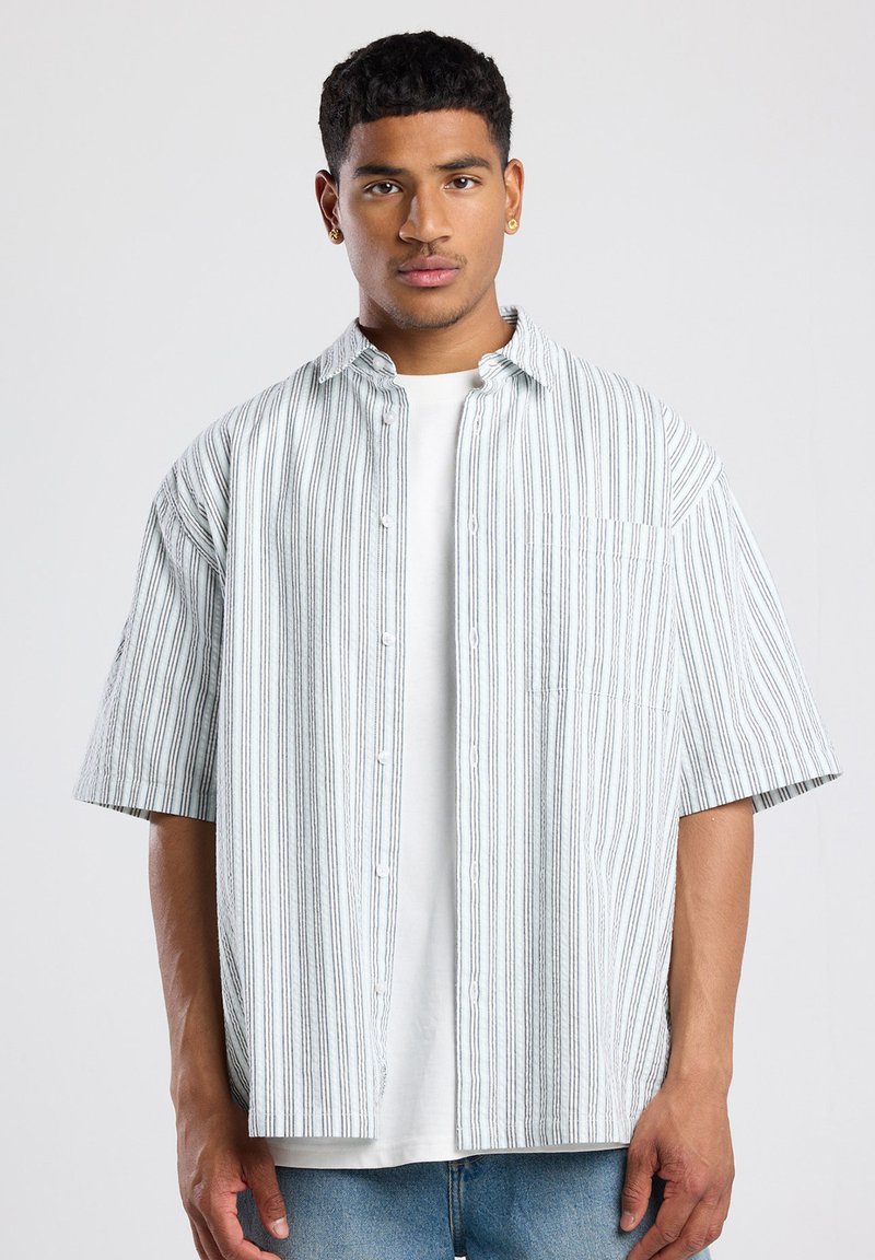 Short-sleeve button-up shirt in white with vertical blue stripes. Features a chest pocket and relaxed fit, made from a lightweight fabric.