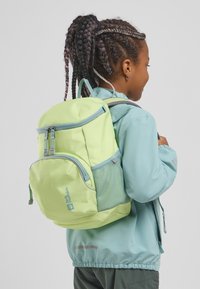 Zaino verde con accenti di verde più chiaro, dotato di molteplici compartimenti con cerniera e una tasca laterale in rete, indossato sulla schiena di un bambino.