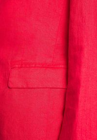 Red linen blazer with a smooth texture, featuring a Single chest pocket and clean stitching along the edges.