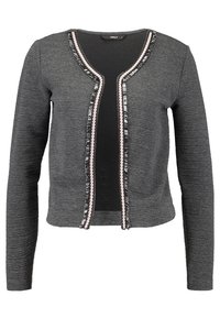 Šedý cardigan s dlouhými rukávy, texturovaná látka, otevřený přední díl a kontrastní lemování s cik-cak vzorem a detailními třásněmi podél okrajů.