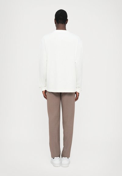 White long-sleeve shirt, brown tailored pants, and white sneakers. Smooth fabric with a relaxed fit, straight-cut design. Minimalist style.