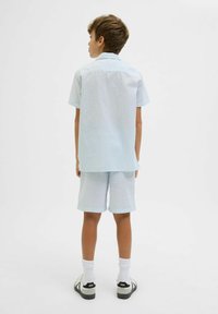 Ensemble de chemise à manches courtes et de shorts bleu clair, avec un motif texturé. Associé à des chaussettes blanches jusqu'à la cheville et des sandales noires.