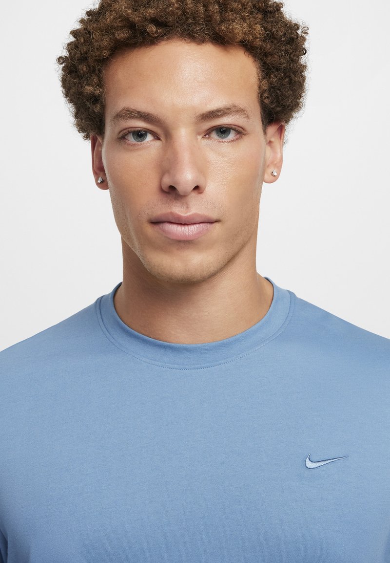 Jasnoniebieska bawełniana koszulka z okrągłym dekoltem, z małym logo Nike na lewej piersi. Gładka faktura, luźny krój.