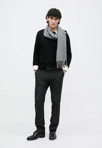Black sweater over a white collared shirt, gray scarf with fringe, gray trousers, and black shoes. The overall look is neutral and simple.