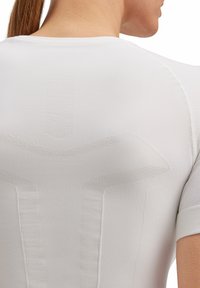 White athletic top featuring textured patterns along the shoulders and back. The material appears smooth with fitted short sleeves.