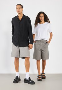 Black long-sleeve button-up shirt, gray shorts, white t-shirt, gray shorts; black shoes, white socks, black sandals; smooth textures.