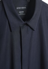 Camisa azul marino con cuello clásico, fabricada en una suave mezcla de algodón, que presenta un pliegue delantero y etiqueta de la marca en el cuello. Diseño de corte regular.