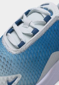 Κοντινό πλάνο μπλε και λευκού αθλητικού παπουτσιού με υφασμάτινο άνω μέρος με υφή και λευκά κορδόνια περασμένα από μπλε ρουθούνια.