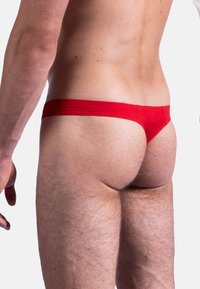 Rote Tanga-Unterwäsche mit gerippter Textur und dünnen Trägern, die ein enges Design und minimale Bedeckung aus seitlicher Perspektive zeigt.