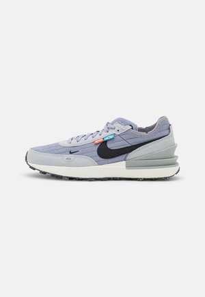 Jasnoszary i lawendowy sneaker z czarnym logo typu swoosh, wyściełanym kołnierzem, teksturowaną podeszwą i małymi pomarańczowymi i niebieskimi metkami przy sznurowadłach.
