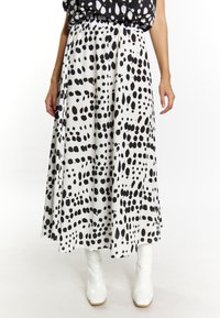 Jupe longue noir et blanc avec un motif à pois, dotée d'une taille élastique et d'un tissu fluide. Portée avec des bottines blanches brillantes.