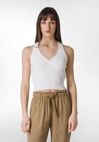 Top corto blanco acanalado con escote en V y diseño sin mangas, combinado con pantalones marrones con cordón que tienen un ajuste relajado y una cintura elástica.