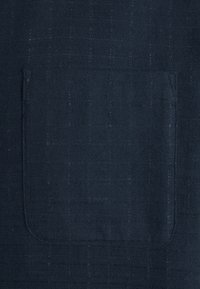 Námornická tkanina s texturovanou vazbou, která má na přední straně našitou náprsní kapsu. Povrch ukazuje jemný vzor a měkký povrch.