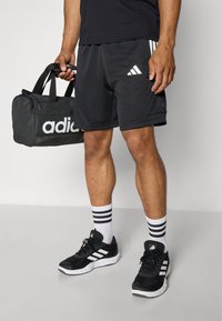 Black athletic shorts with white stripes and logo, black sports shoes with white accents, and a black duffel bag featuring a large white logo.