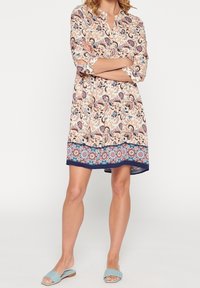 Blumengemustertes Kleid in hellbeige mit Dreiviertelärmeln und navyfarbigem Saum. Kombiniert mit hellblauen Rutschsandalen.