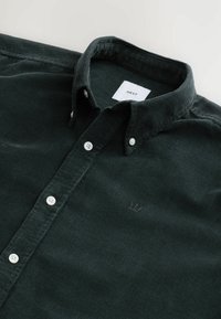 Dark green corduroy shirt with a button-down collar, white buttons, and a small embroidered logo near the hem. Tag reads 'NEXT.'