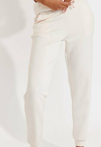 Cremefarbene Jogginghosen aus weichem Material mit einem elastischen Bund und pinkem Kordelzug, seitlichen Taschen und gerippten Bündchen.
