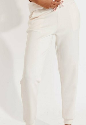 Cremefarbene Jogginghosen aus weichem Material mit einem elastischen Bund und pinkem Kordelzug, seitlichen Taschen und gerippten Bündchen.