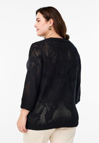 Pull en maille noire avec un motif en dentelle florale, doté de manches trois-quarts et d'un ourlet côtelé, présentant une coupe décontractée et un design texturé.