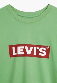 Zelené bavlněné tričko s kulatým výstřihem. Na jeho přední straně je velký červený obdélníkový logo s nápisem "LEVI'S" v bílých velkých písmenech. Měkká textura.