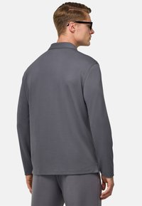Graues Langarm-Polohemd mit klassischem Kragen, glatter Textur, geradem Saum und minimaler Nähdetails, kombiniert mit passenden Hosen.