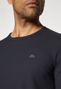 Marineblaues, geripptes Langarmshirt mit Rundhalsausschnitt und kleinem, tonal gehaltenem Logo auf der Brust. Der Stoff wirkt strukturiert und enganliegend.