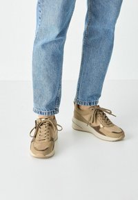 Sneaker beige con una combinazione di suede e pelle, design con lacci e suola a zeppa. Jeans con un leggero risvolto completano il look.